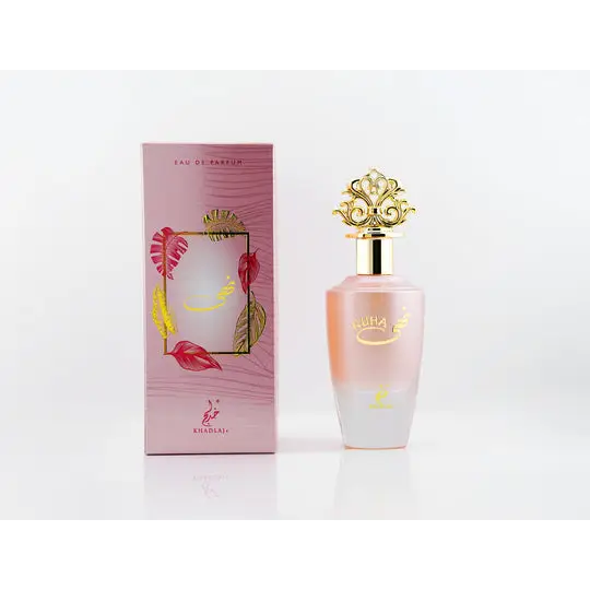 A pink gradient glass perfume bottle with a gold ornate cap and kuha branding beside a matching tropical leaf box